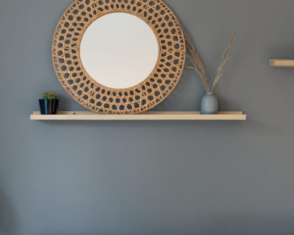 A vertical shot of room decor with a round woven frame with a white center and reed in a vase hanging on a wall